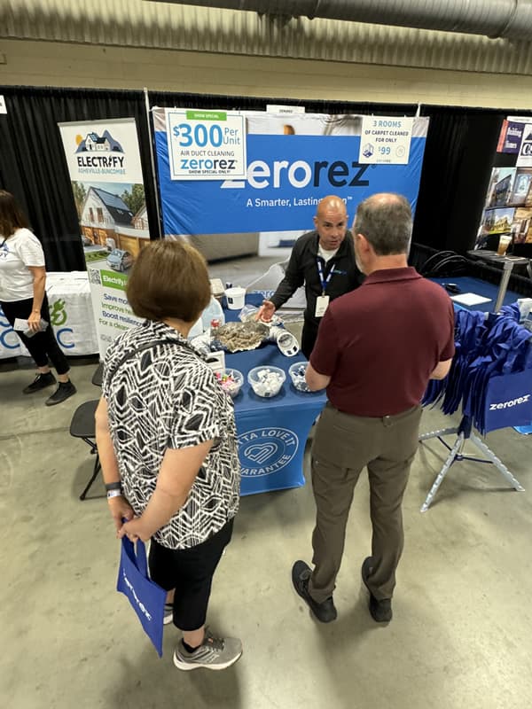Man speaking with man and women in front of Zerorez table.