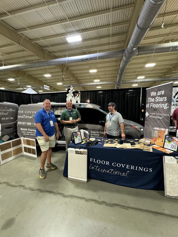 Three men behind "Floor Coverings International" table.