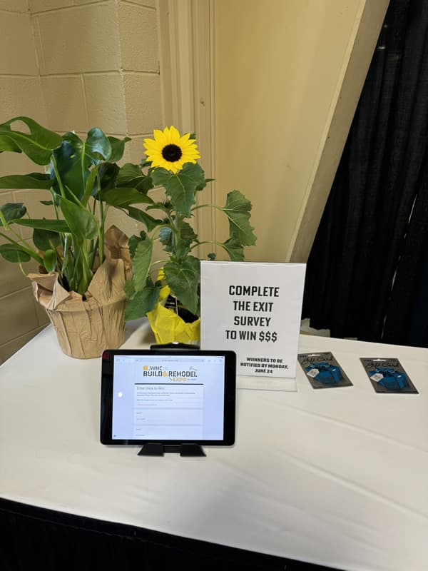 Sunflower on table with "Complete the exit survey to win $$" sign and an iPad with "WNC Build & Remodel."