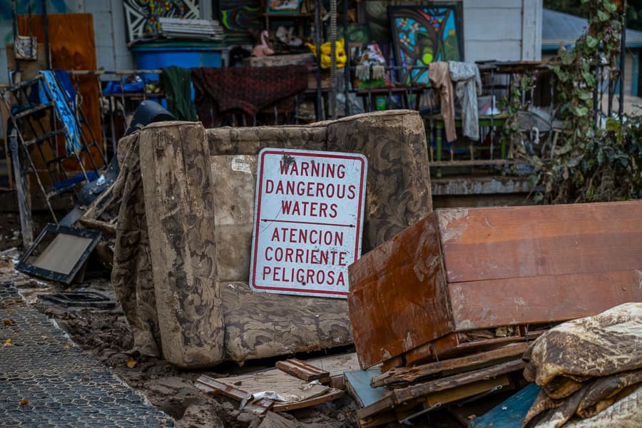 Hurricane Helene wreckage with furniture on the street and a "Warning Dangerous Waters" sign.