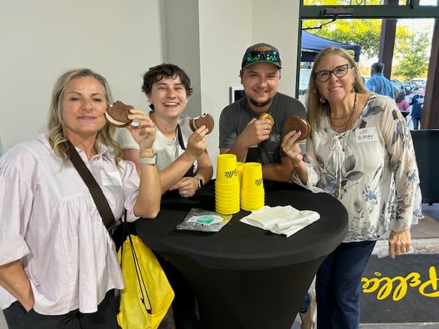Four women eating ice cream sandwiches smiling at the camera.