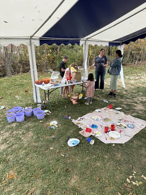 Kids tent with children at the table and blanket in the grass with art supplies.