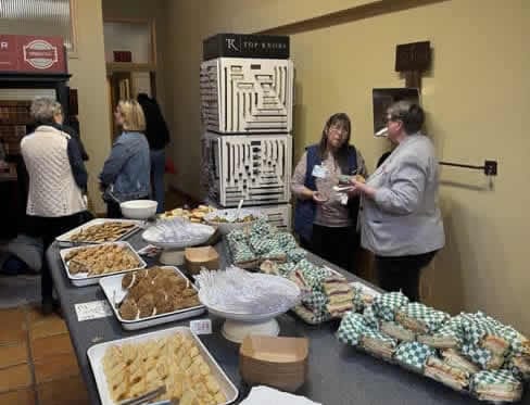 Two women talking near food table.