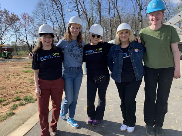 5 women wearing hard hats arm in arm for photo.