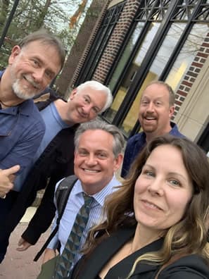 Four men and one women taking selfie in front of building.